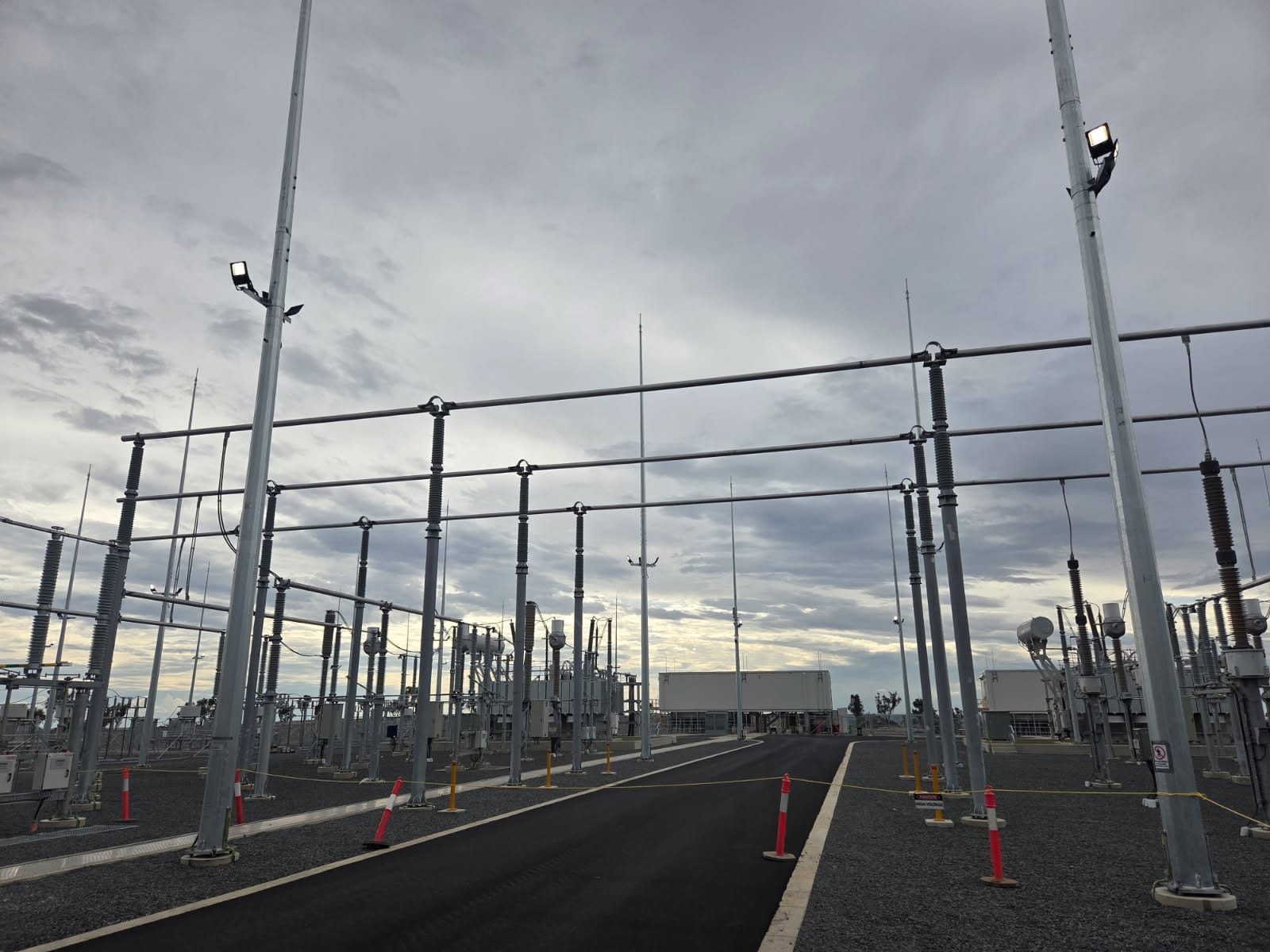 Wide landscape view down the sealed access road through the completed switchyard, gantries and disconnector stacks eithe