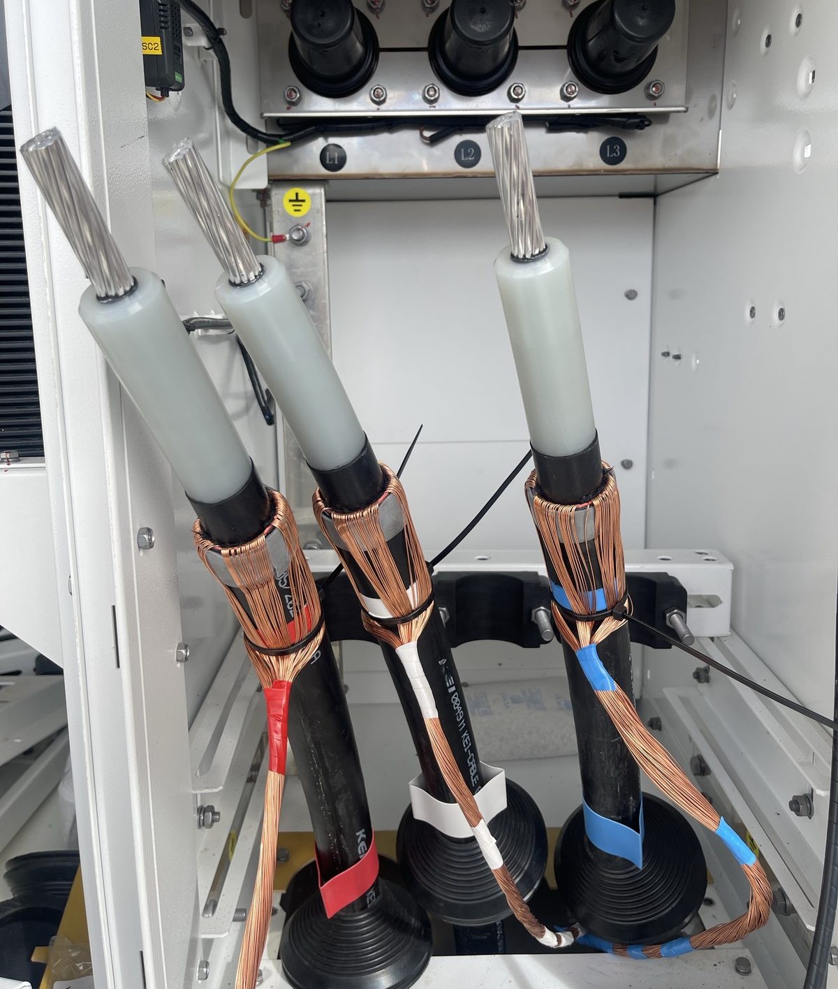 Most dramatic shot: three 33kV elbow terminations mid-assembly in a ring main unit, copper screen wires fanned back over