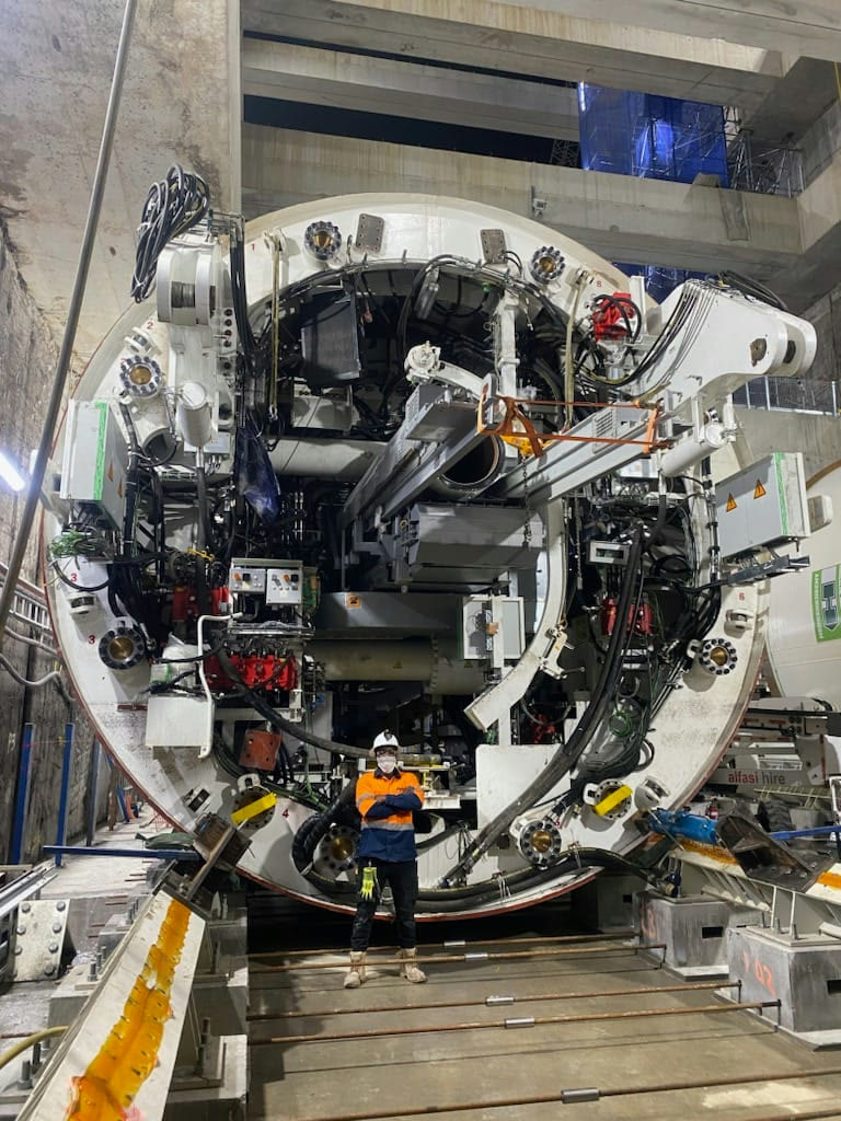 Giidjaa team member Aiah standing arms crossed in front of the fully assembled TBM cutterhead in the launch box