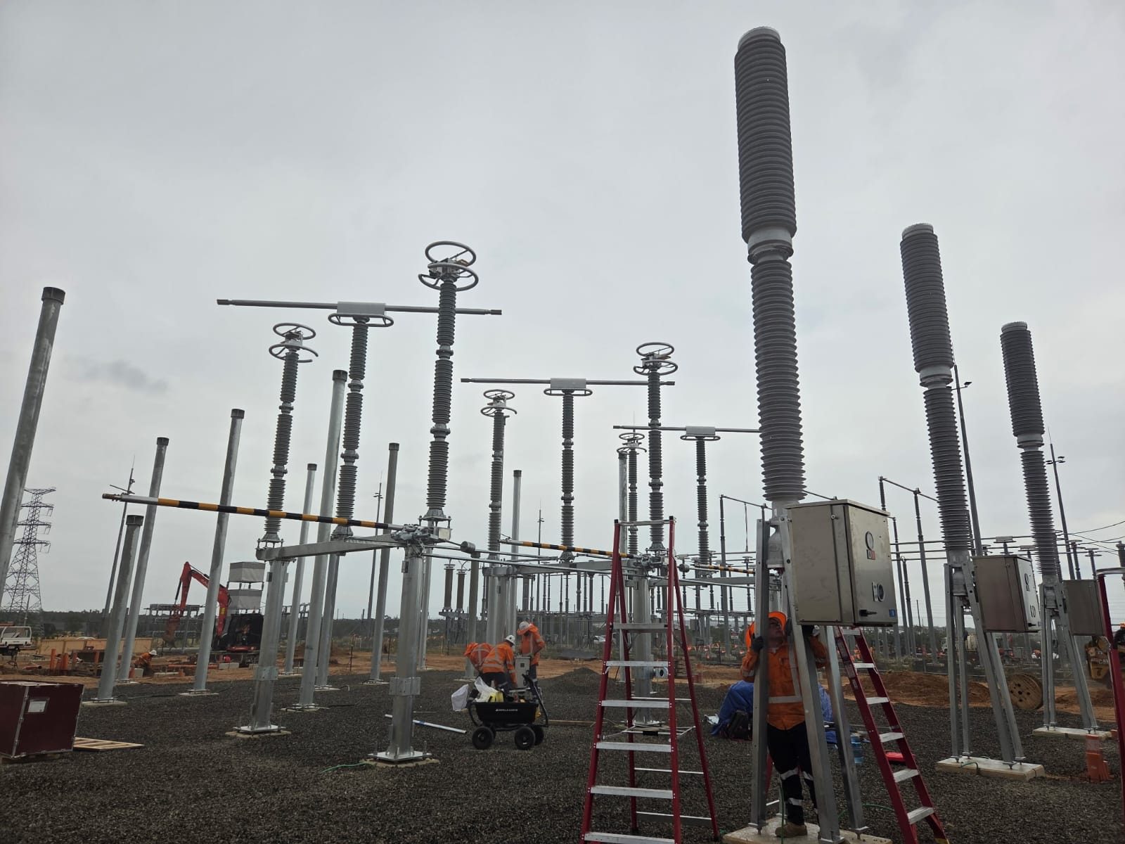 HERO — switchyard under construction at ground level: galvanised steel structures and tall grey insulator stacks, crews