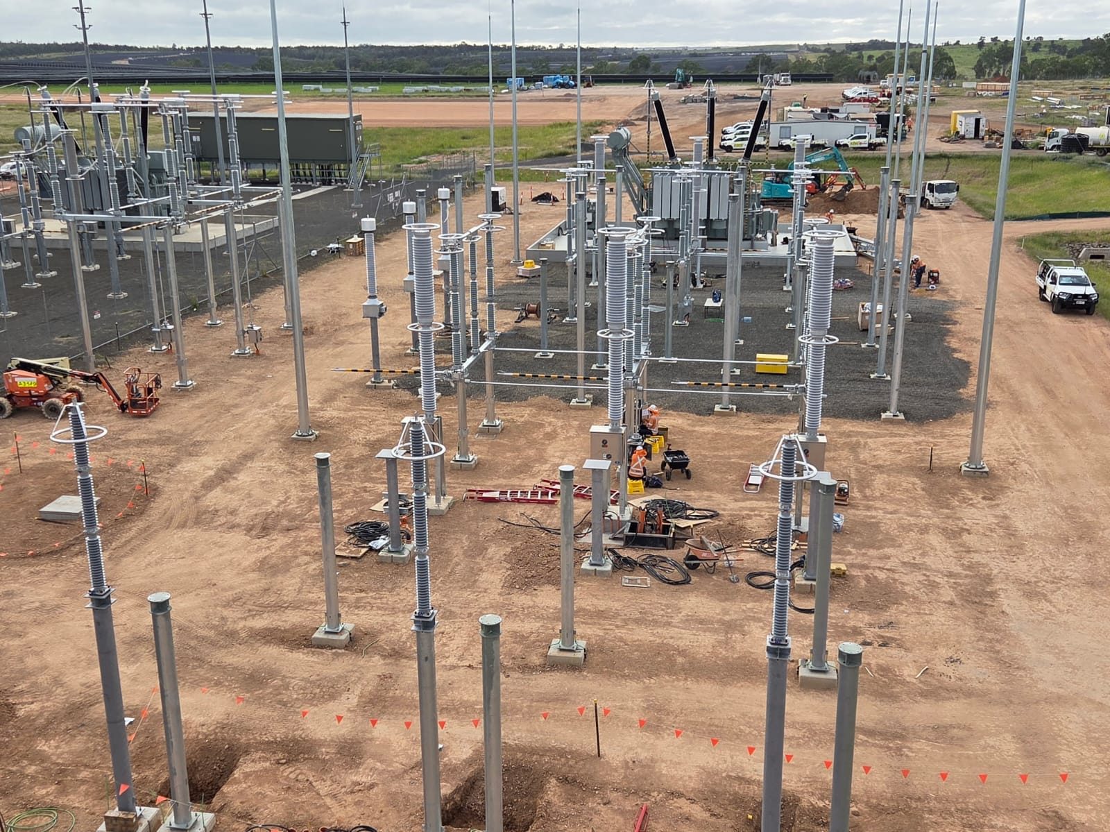 Elevated wide overview of the South Bay works — steel structures and insulator stacks rising from red dirt, plant and cr