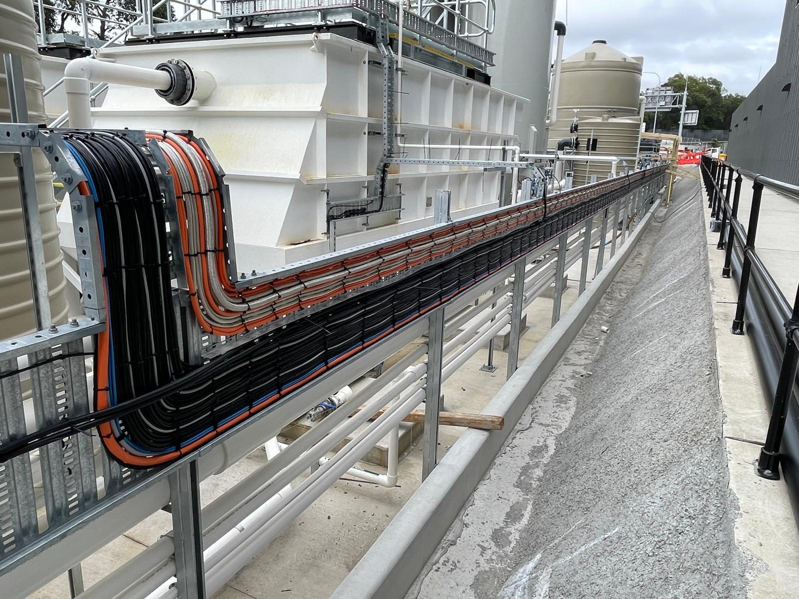 Landscape hero-quality shot: long run of neatly dressed cable ladder with orange HV conduits and black cabling sweeping